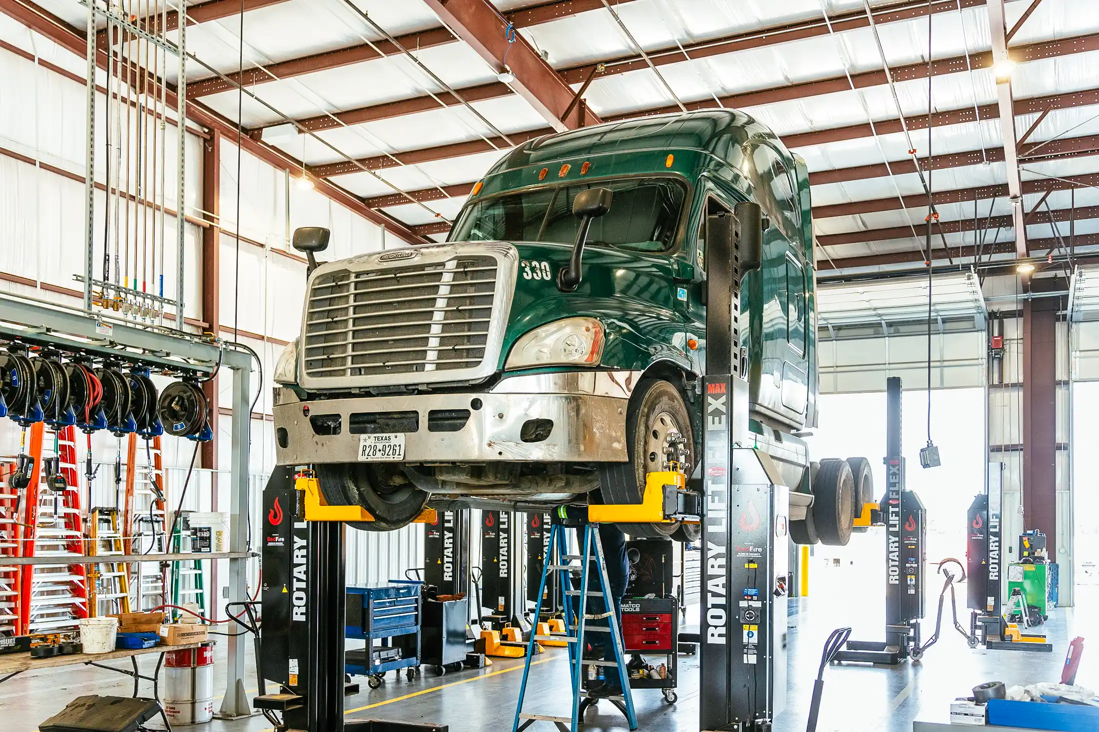 Green semi-truck on a Rotary lift in repair facility